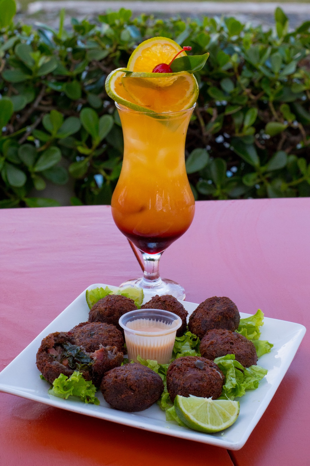 Drinque cítrico em camadas laranja e vermelho, servido com bolinhos crocantes