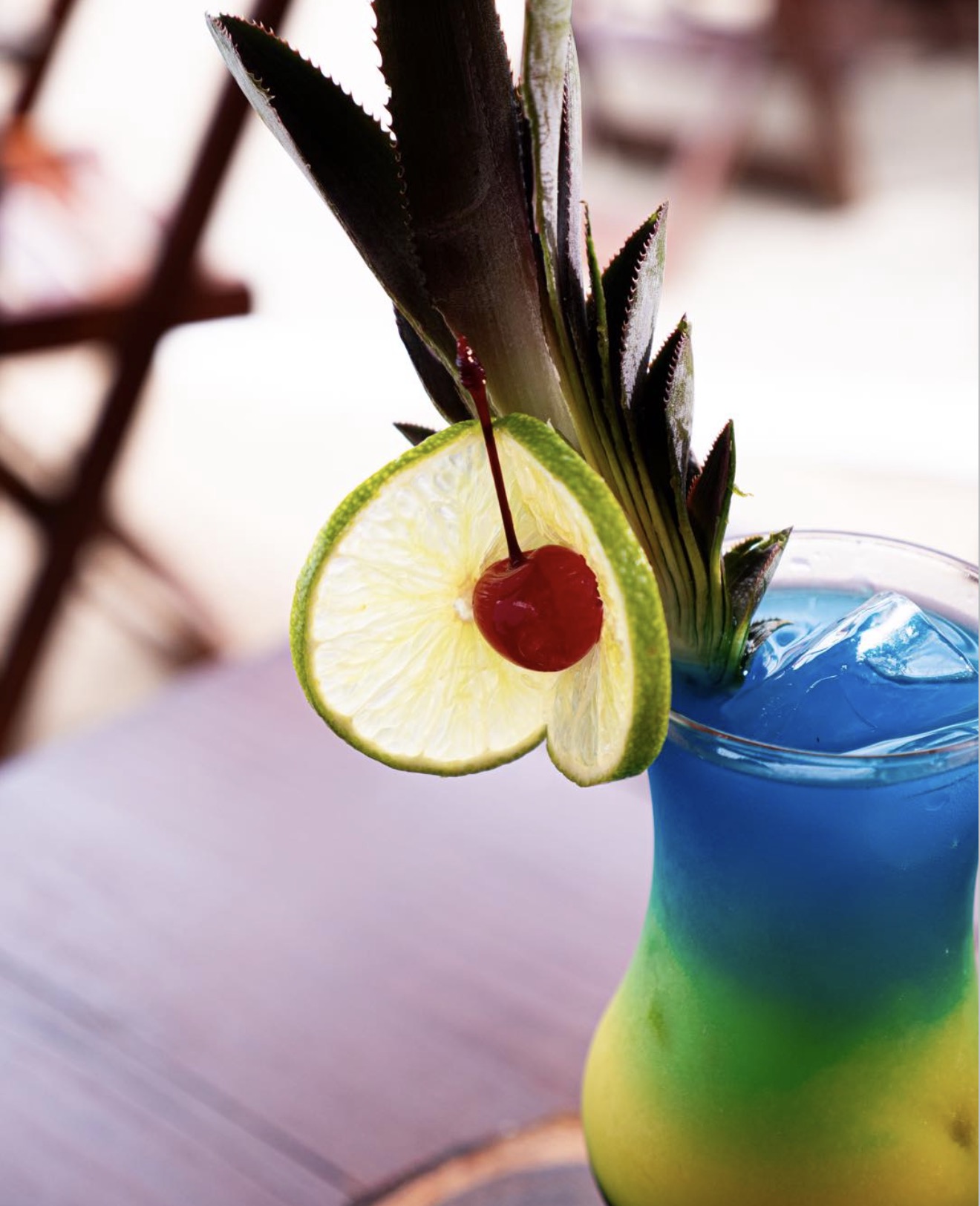 Drinque tropical em camadas azul e amarela, decorado com limão, cereja e folha de abacaxi