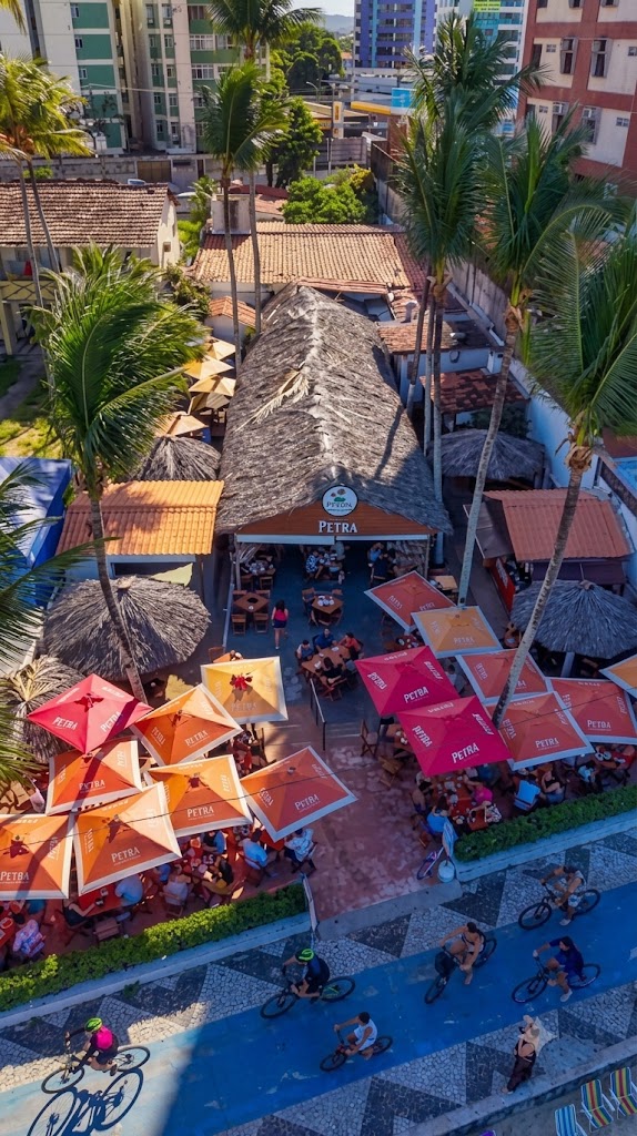 Vista aérea do Fruta Pão: telhado de palha, guarda-sóis laranja e vermelhos, coqueiros e o calçadão da praia de Candeias